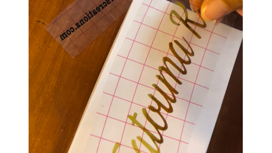 Handwriting practice sheet with 'Autumn' on grid paper, tape, and pen visible.