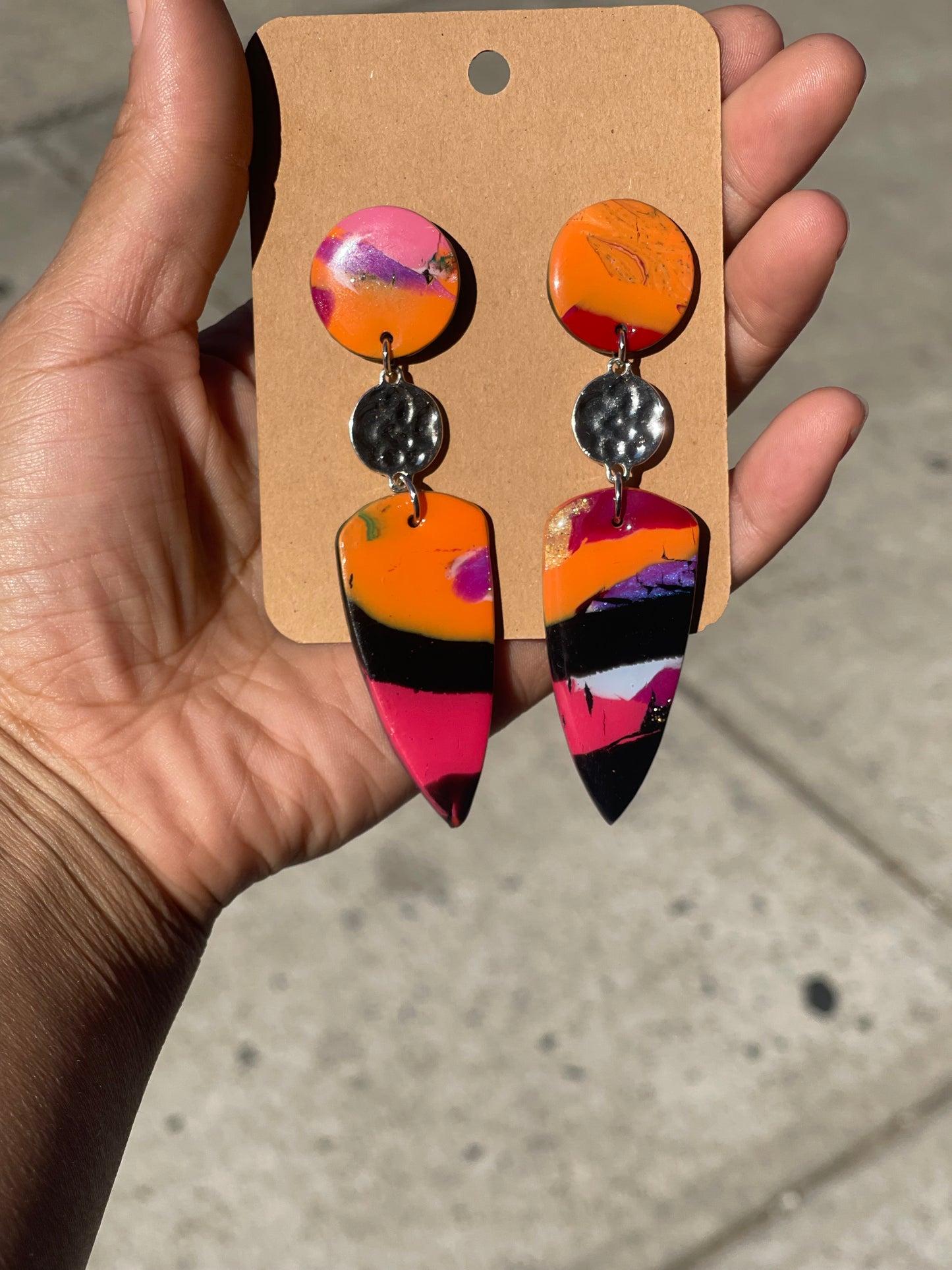 Colorful earrings on a wooden display card held by a hand against a neutral background
