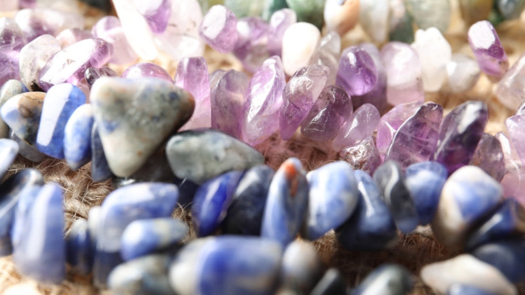 Close-up of various colored gemstones including amethyst and lapis lazuli on a textured surface.
