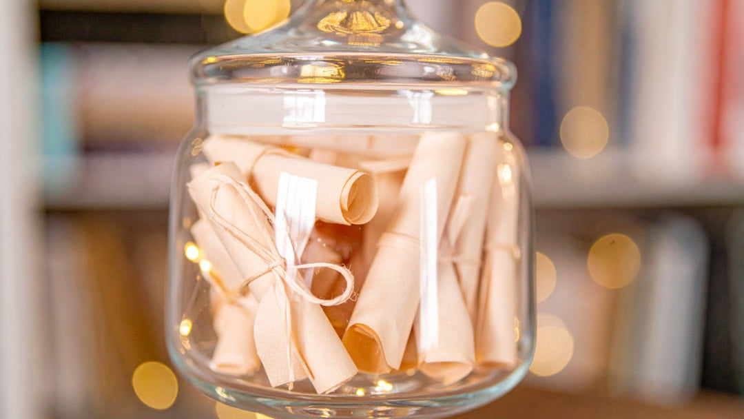 Glass jar with decorative lights filled with cylindrical gift notes, sitting on a blurred background