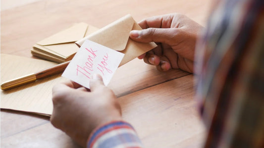 Artist holding a small handwritten card with 'Thank you' on a wooden surface